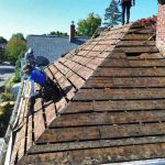 Structural roof repair in progress showing damaged roof decking and professional roofing contractors at work